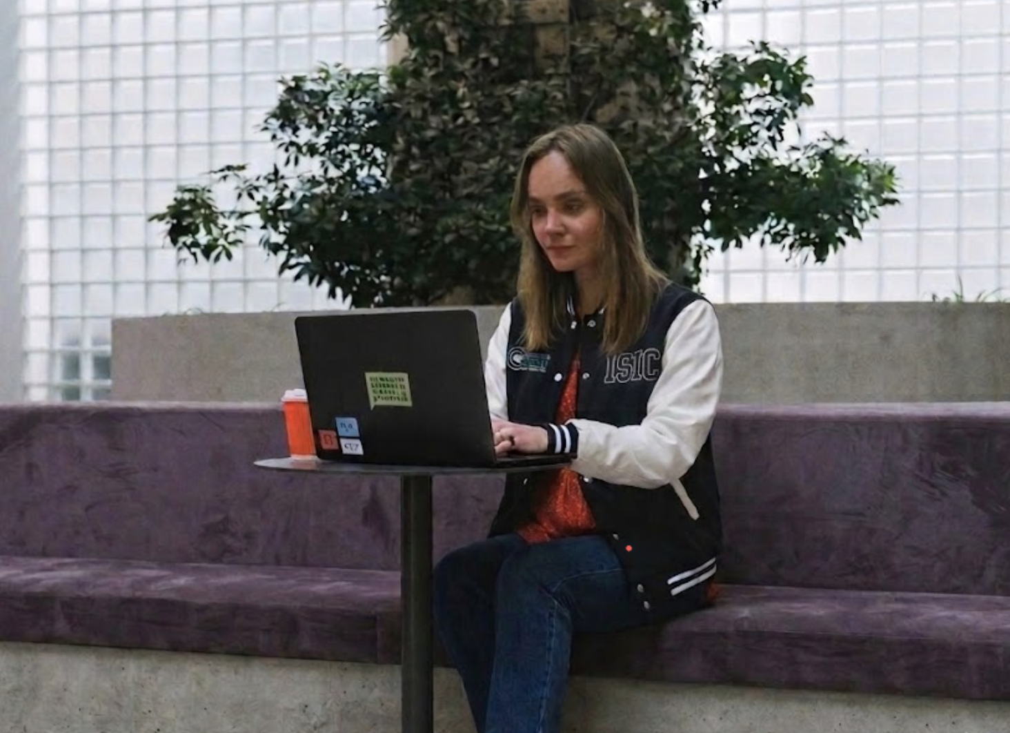 Young woman in red dress using laptop indoors, showcasing remote work lifestyle.
